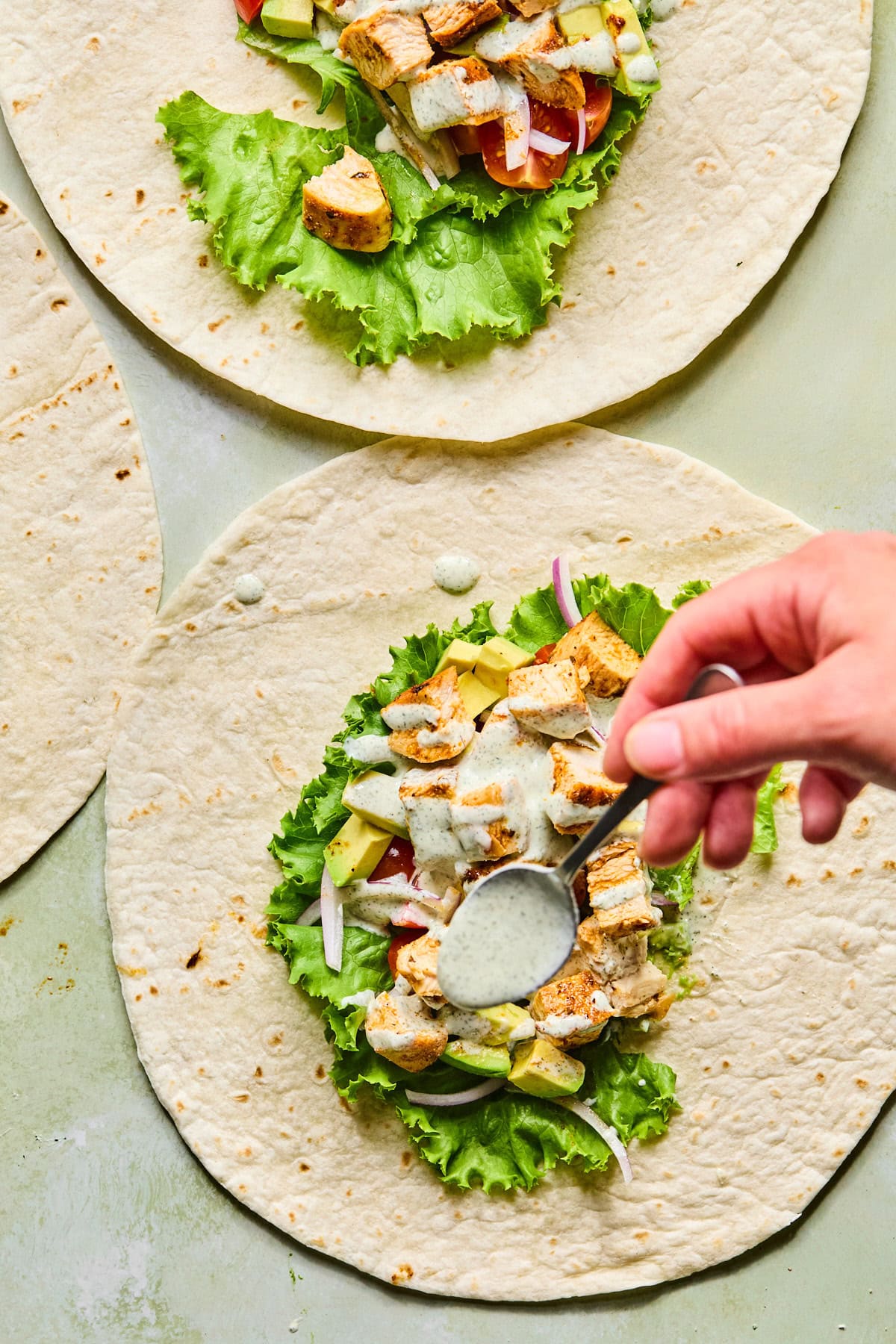 Grilled chicken wrap being drizzled with creamy high-protein ranch dressing before folding.