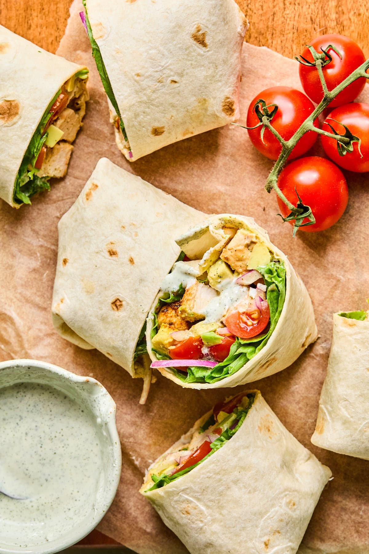 Grilled chicken wraps cut in half and arranged on brown parchment paper, with one turned on its side to show the filling and ranch inside.