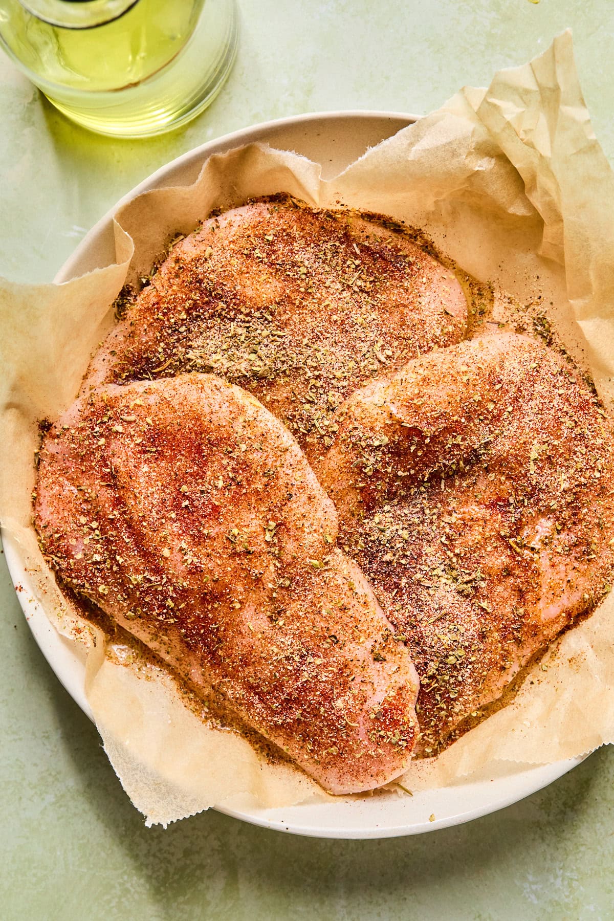 Seasoned chicken breasts in a parchment lined bowl, ready to grill.
