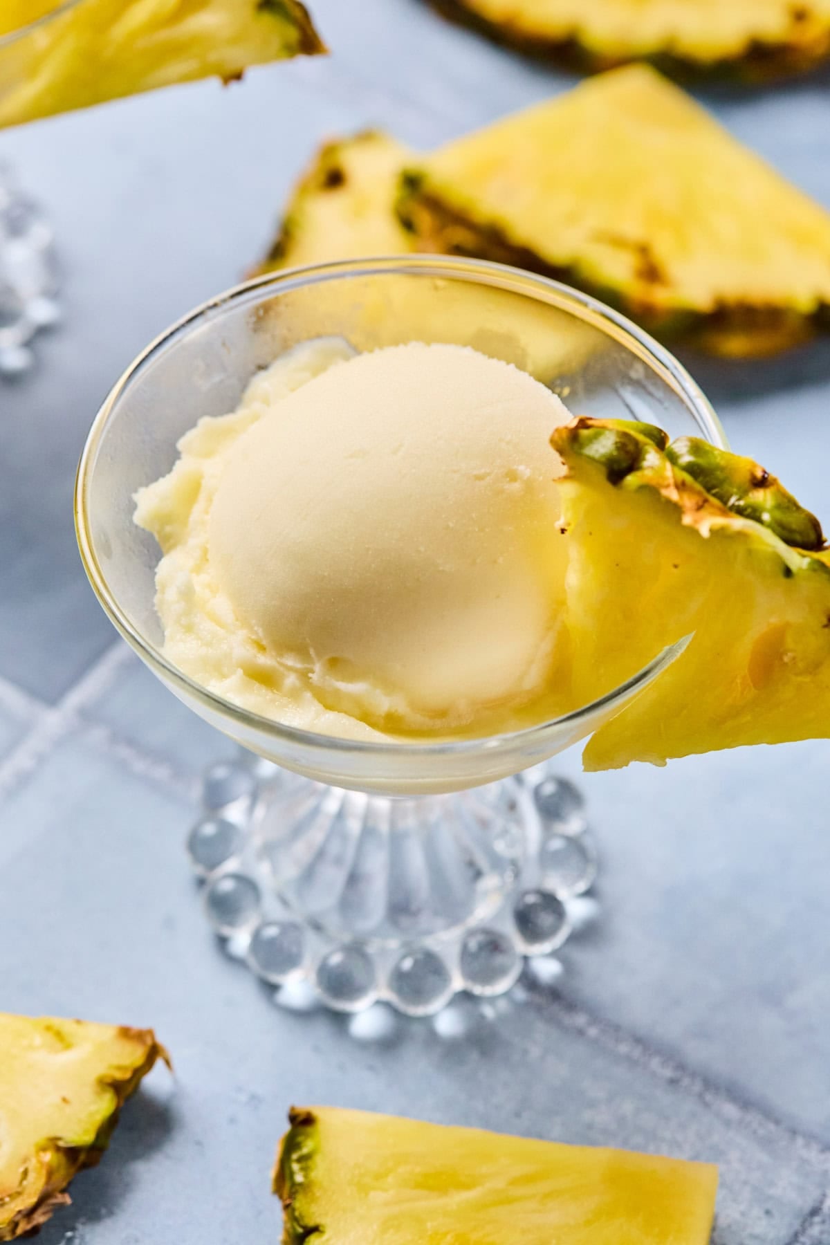 Close-up of Ninja Creami pineapple sorbet in a glass with a fresh pineapple slice on the rim.
