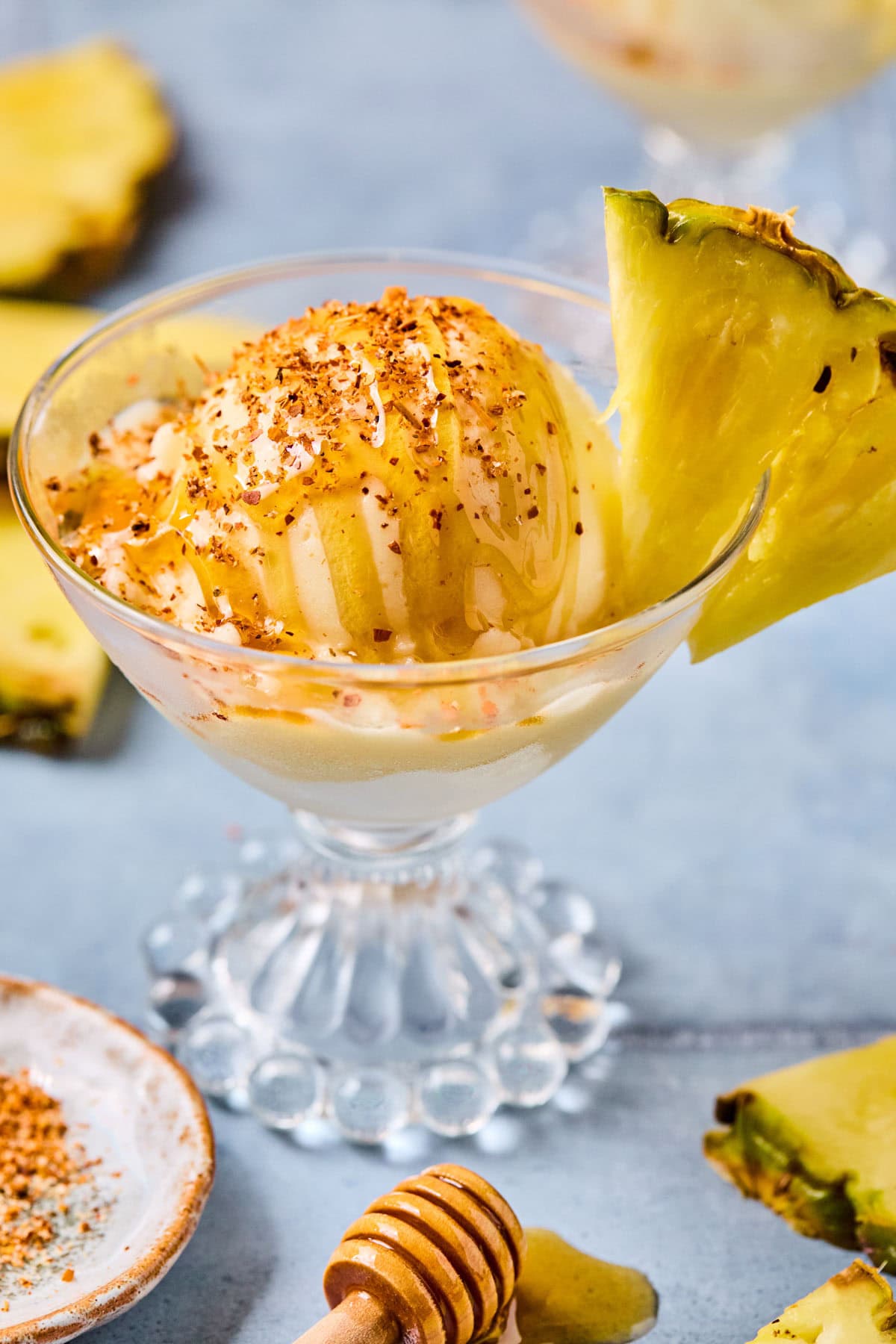 Close-up of a scoop of Ninja Creami pineapple sorbet topped with honey and Tajin in a glass with a pineapple slice on the rim.