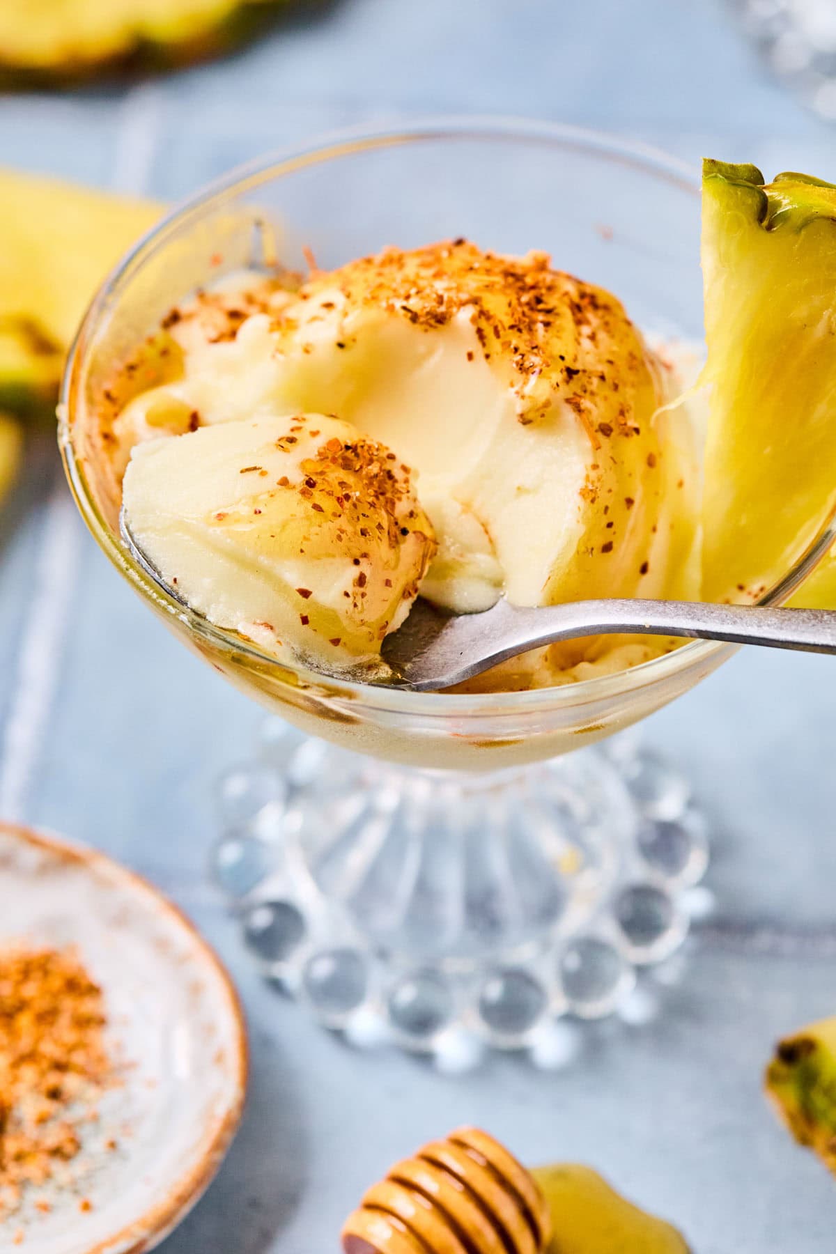 A spoon scooping out a bite of pineapple sorbet with honey and Tajin from a glass with a pineapple slice on the rim.
