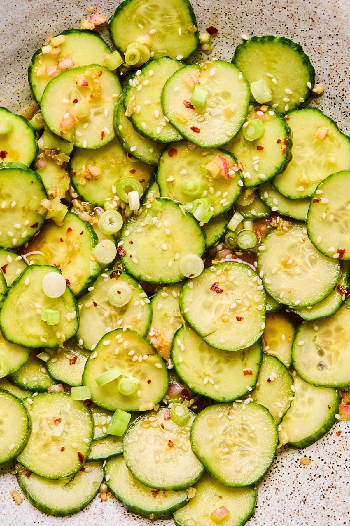Close-up of marinated Asian cucumbers topped with sesame seeds, sliced green onions, and red pepper flakes.