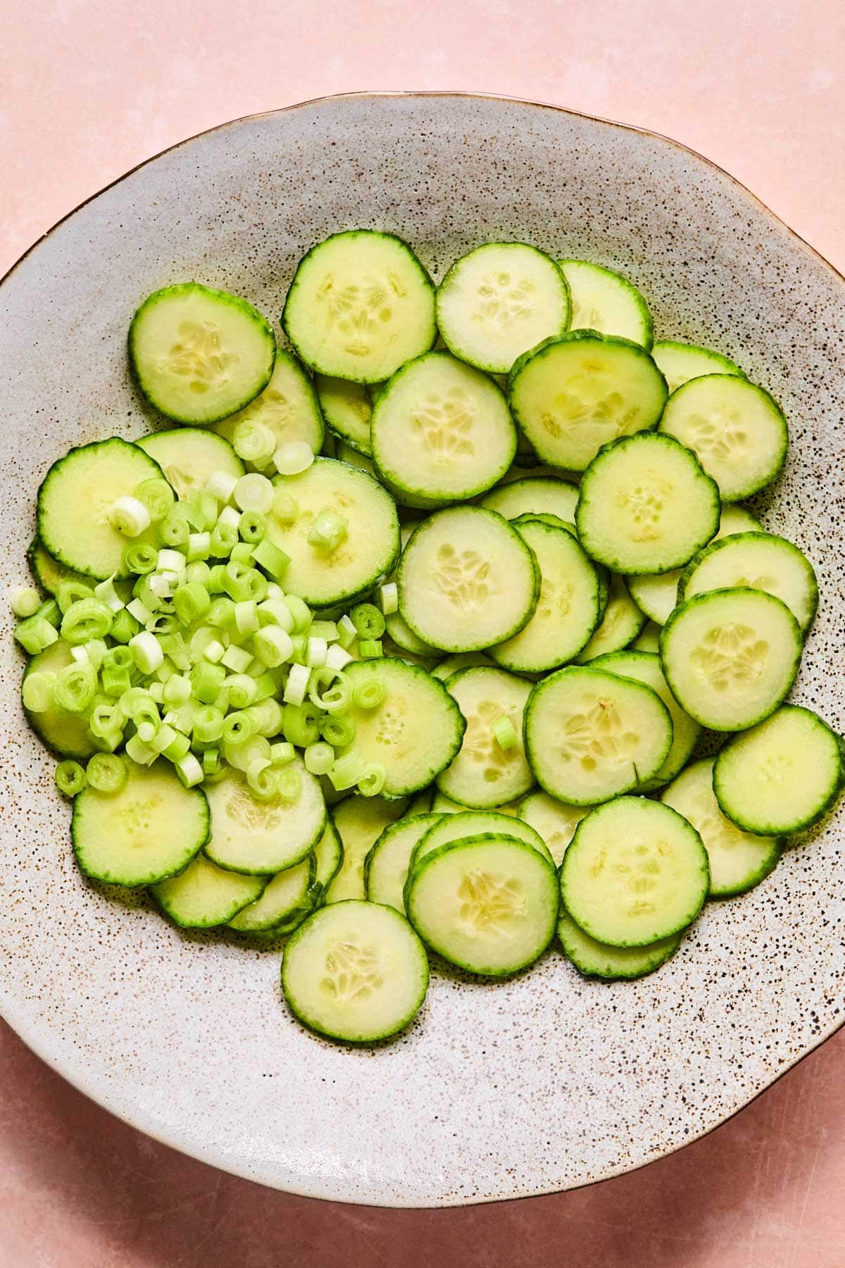 Thinly sliced mini cucumbers and chopped green onions tossed together in a bowl.