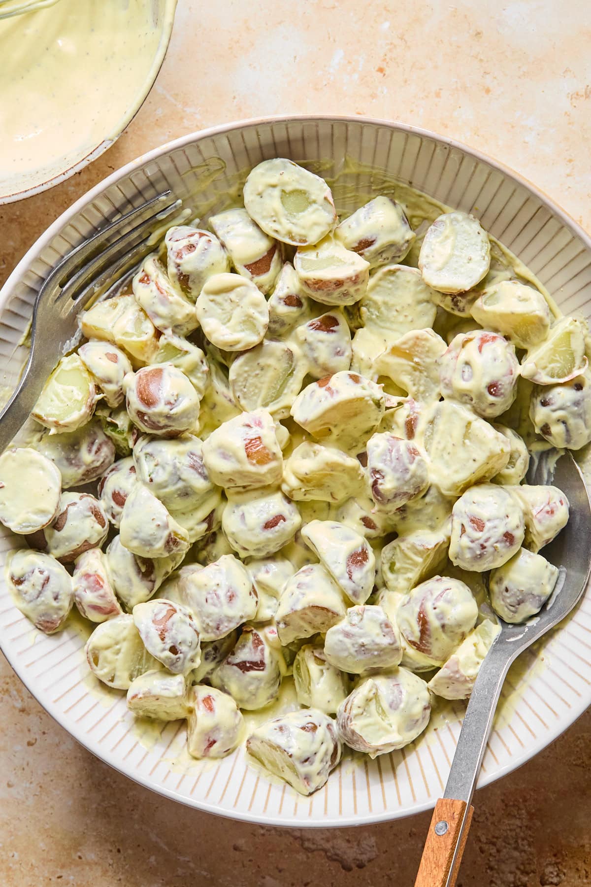 Warm red potato chunks tossed with creamy mustard dressing in a large mixing bowl.