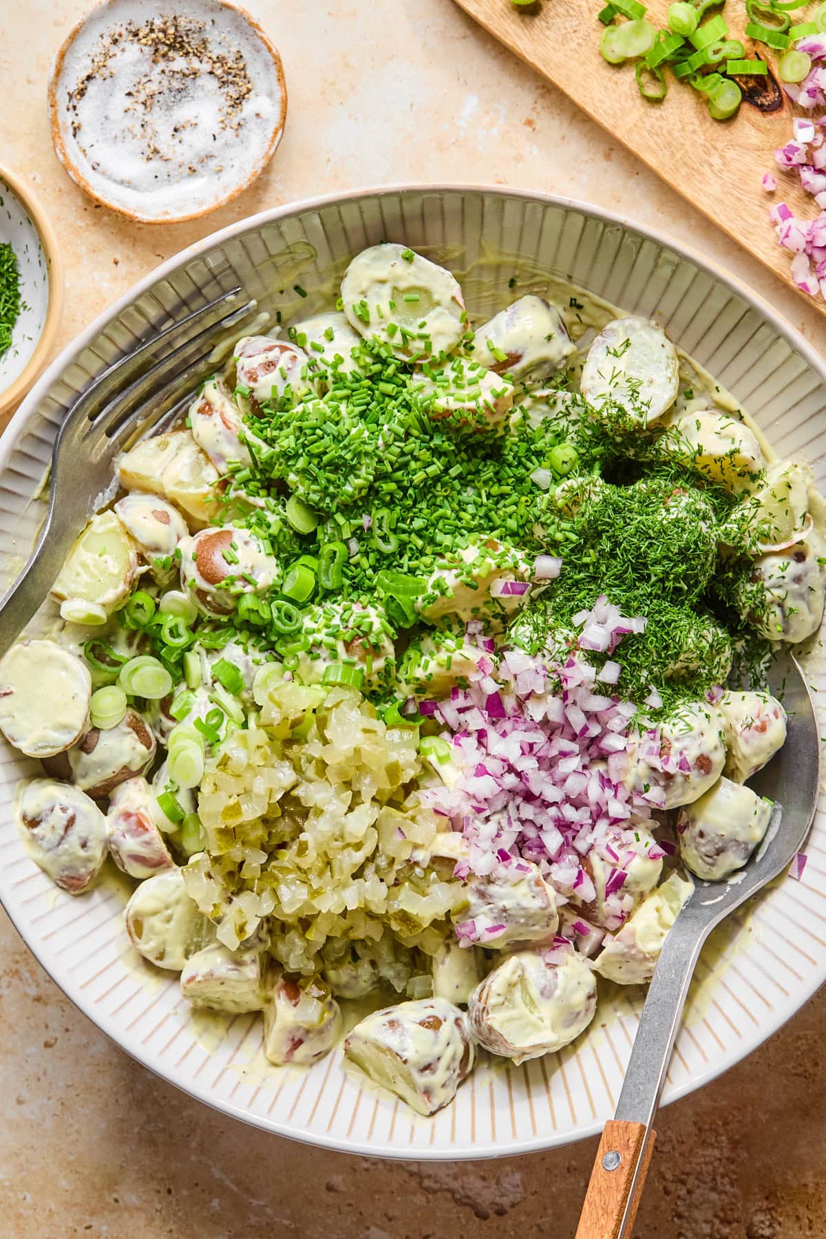 Chopped dill pickles, red onion, green onions, fresh dill, and chives ready to fold into the red potato salad.