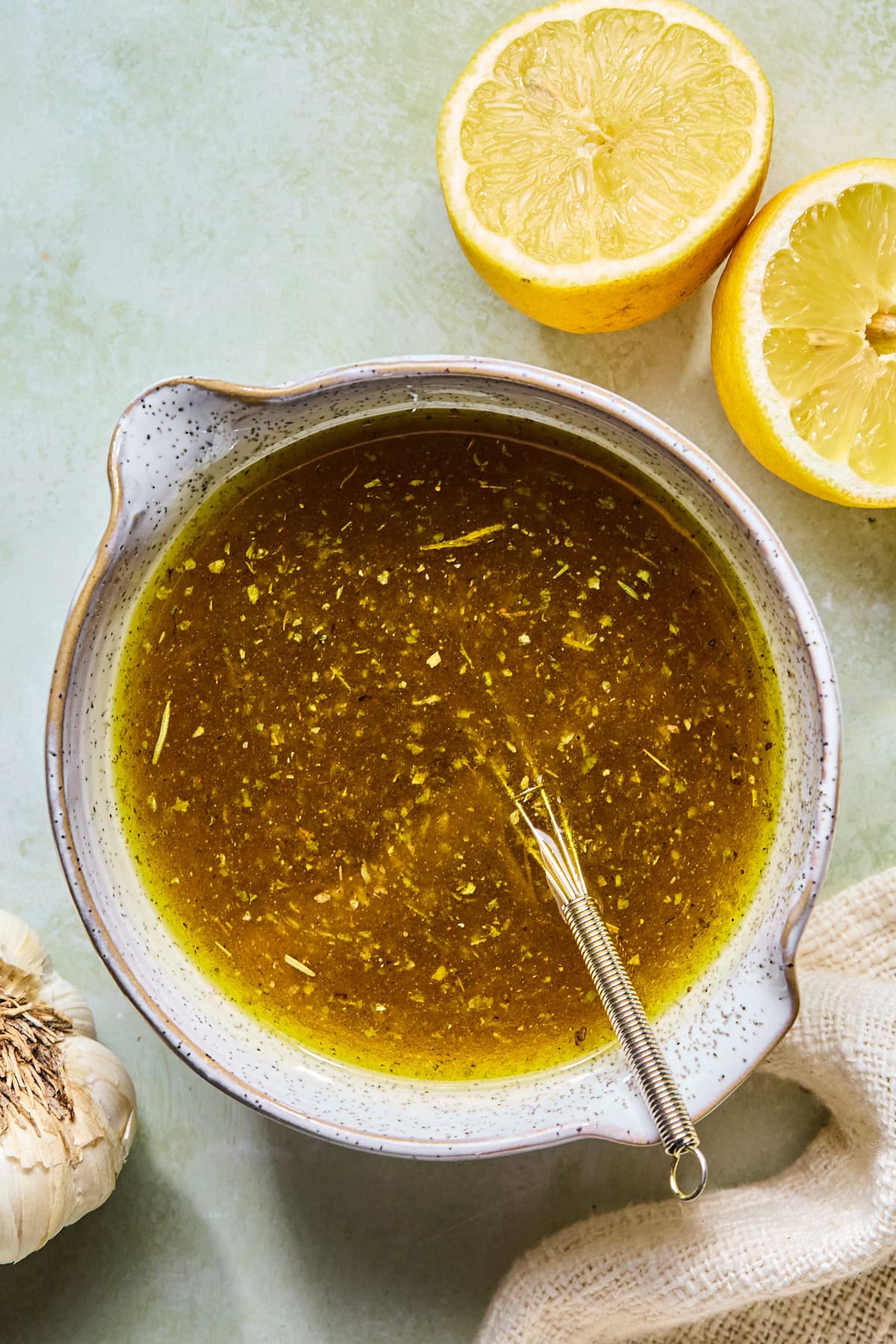 Homemade Italian vinaigrette made with olive oil, red wine vinegar, lemon juice, pepperoncini brine, lemon zest, garlic, and seasonings being whisked together in a glass bowl.