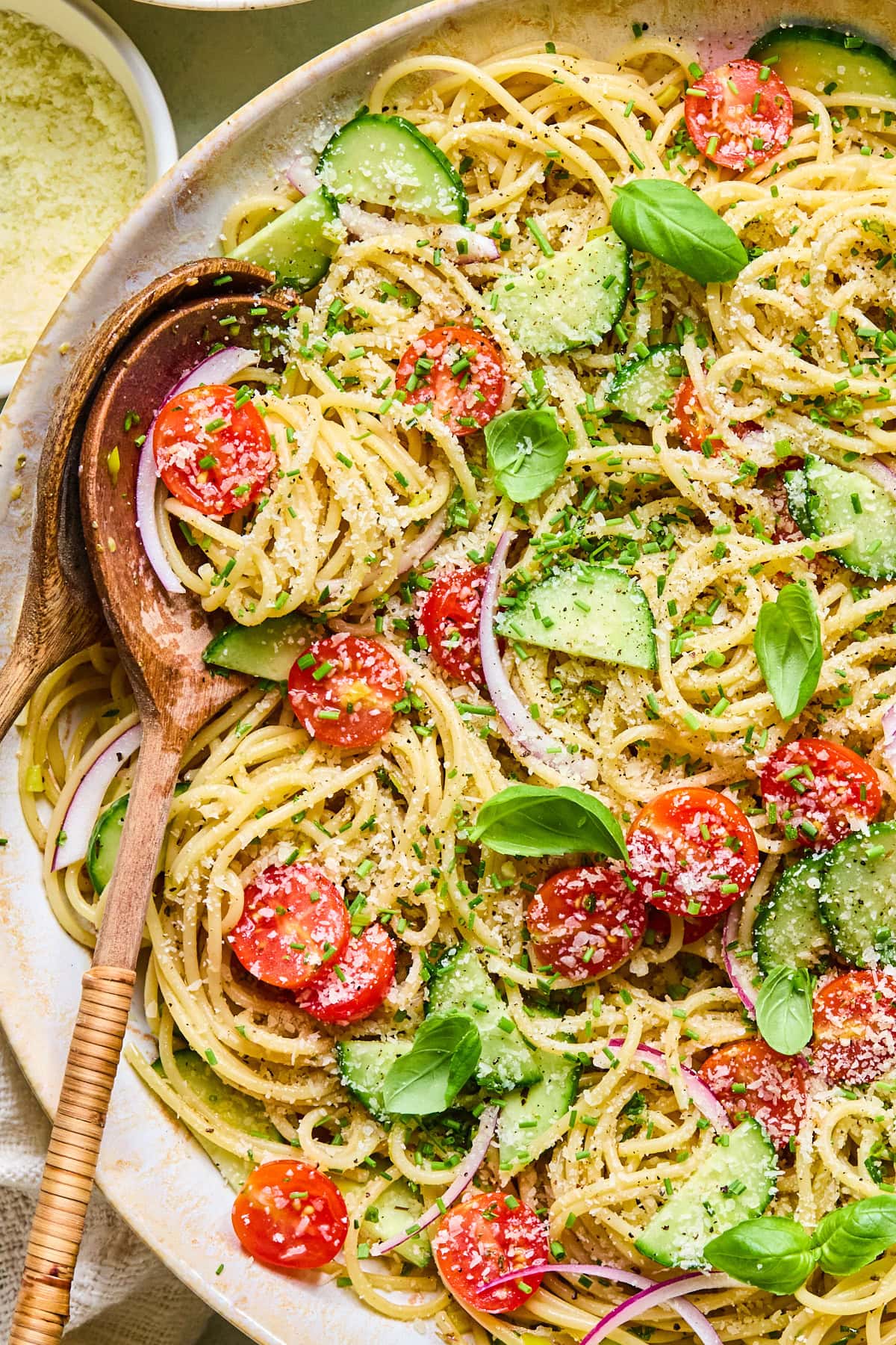 Close-up of spaghetti salad with homemade Italian vinaigrette in a serving bowl topped with Parmesan cheese and fresh herbs, with wooden salad servers inside of the bowl.