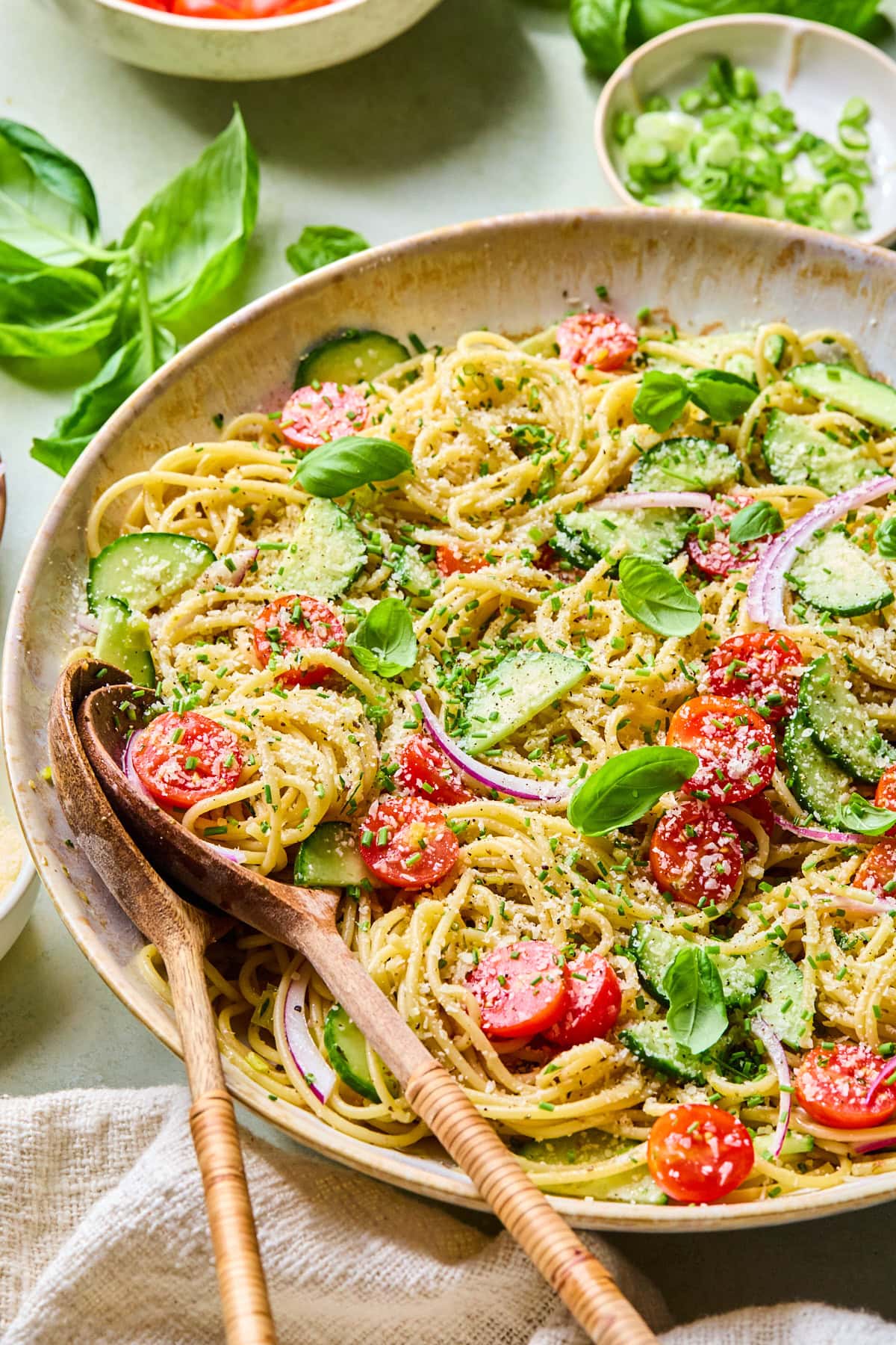 Close-up of spaghetti salad with homemade Italian vinaigrette in a serving bowl topped with Parmesan cheese and fresh herbs, with wooden salad servers inside of the bowl.