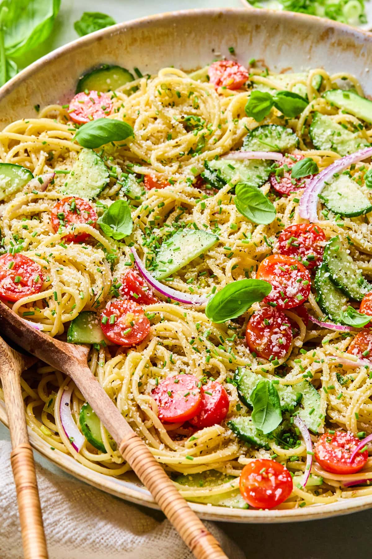 Close-up of spaghetti salad with homemade Italian vinaigrette in a serving bowl topped with Parmesan cheese and fresh herbs, with wooden salad servers on the side of the bowl.