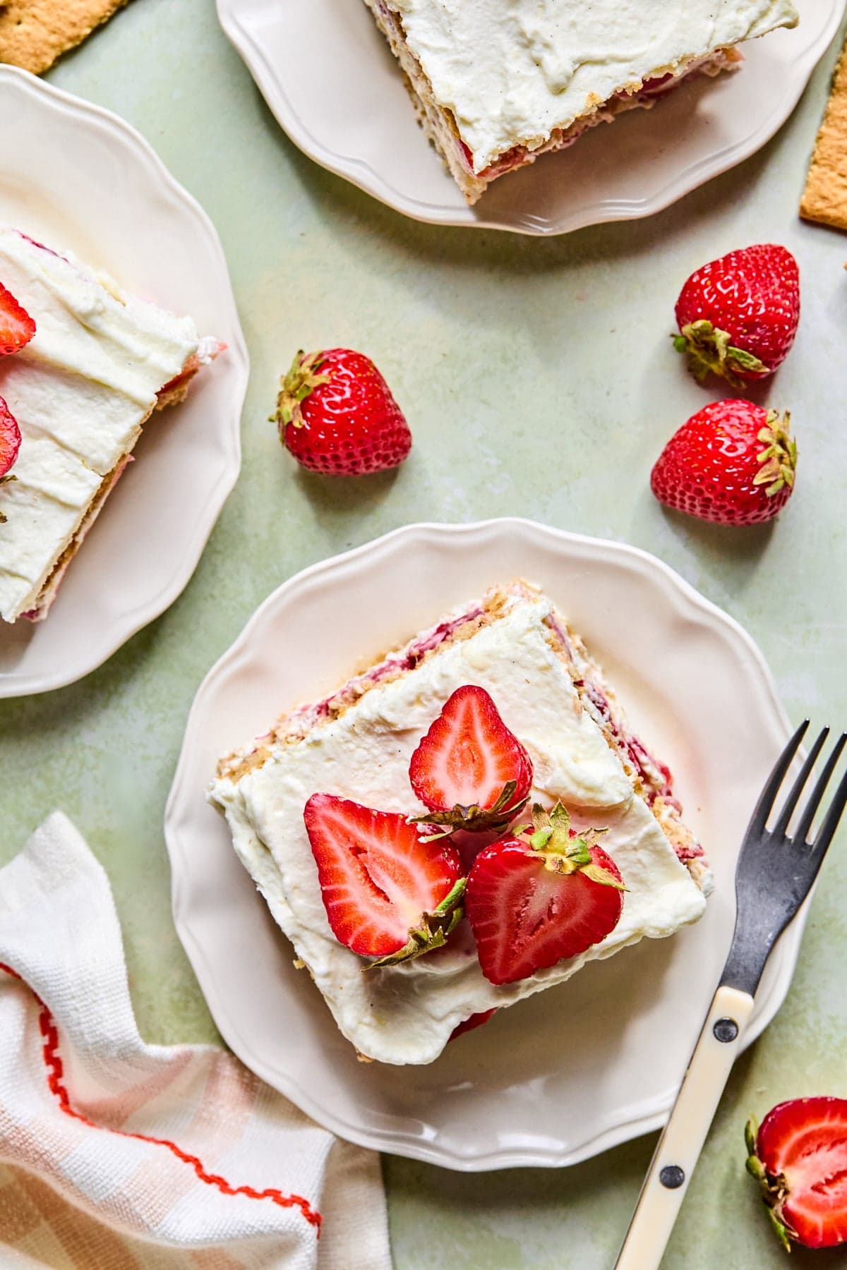 Three plates of strawberry icebox cake topped with fresh strawberries, with a fork resting beside the front plate.