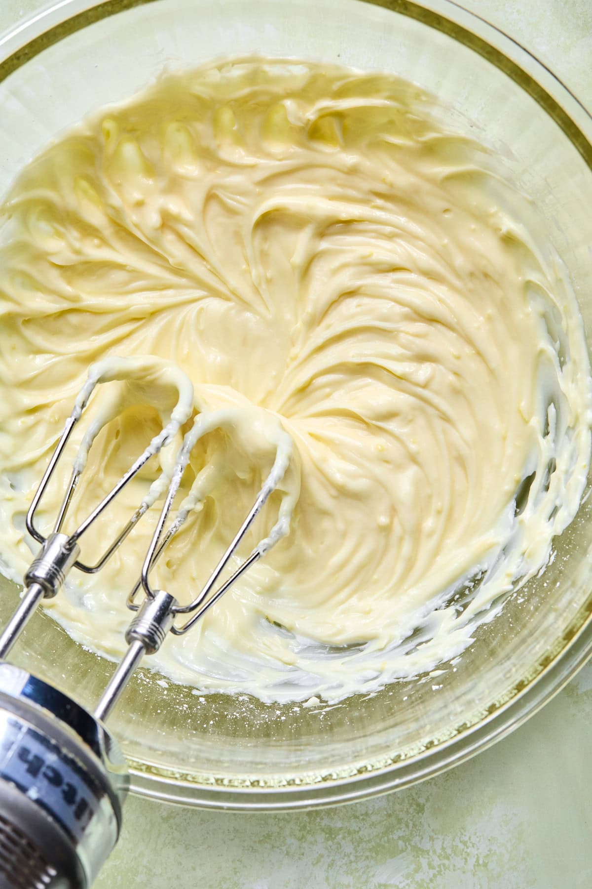 Cream cheese and powdered sugar mixed with a hand mixer in a glass bowl until smooth and creamy.