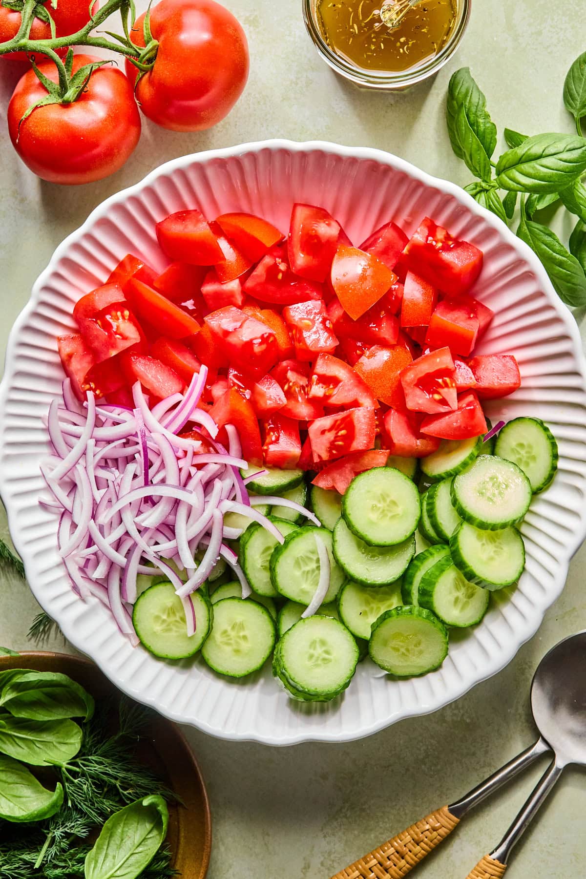 Thick slices of English cucumber, chunky tomatoes, and thinly sliced red onion in a large serving bowl.
