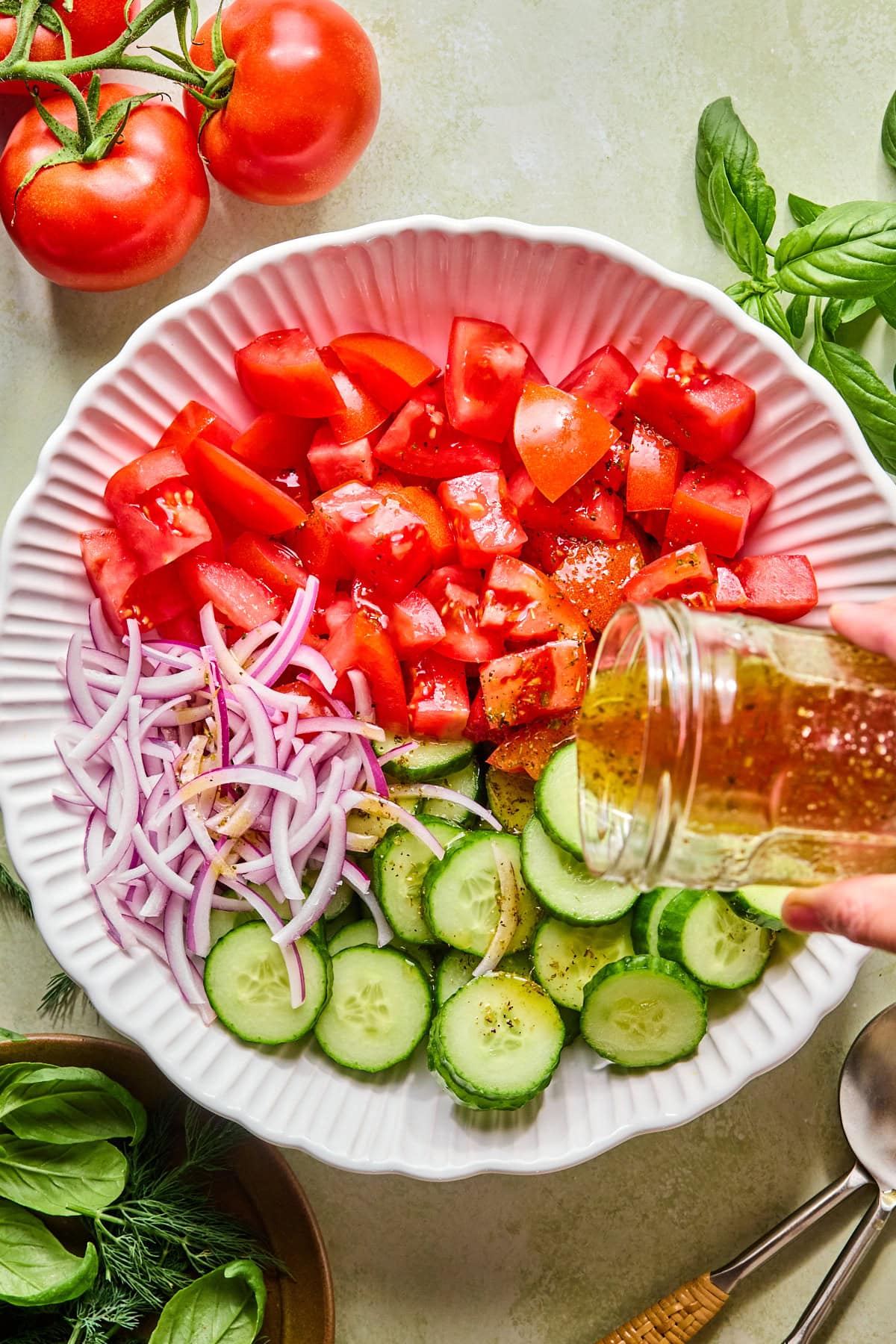 Dressing being poured over cucumber, tomato, and red onion salad before tossing.