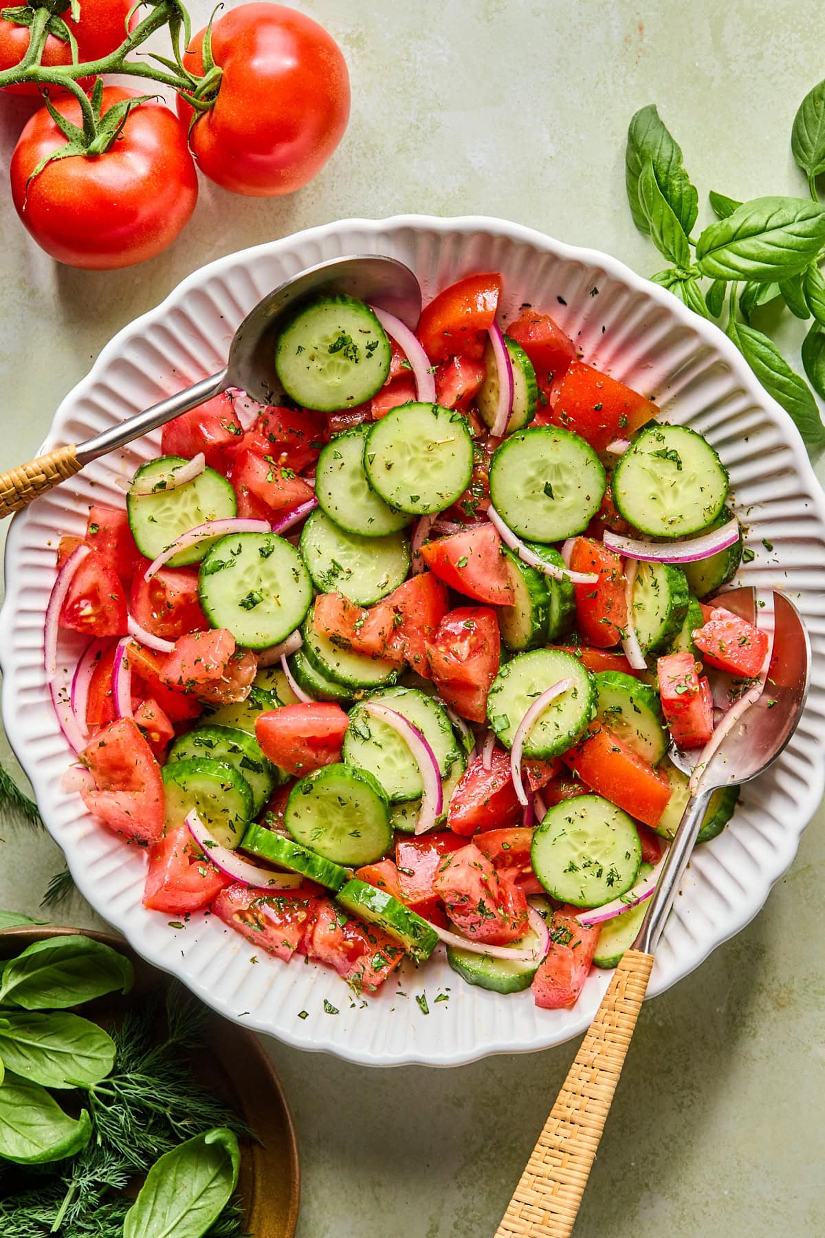 Assembled tomato cucumber salad in a large serving bowl with serving spoons on either side.