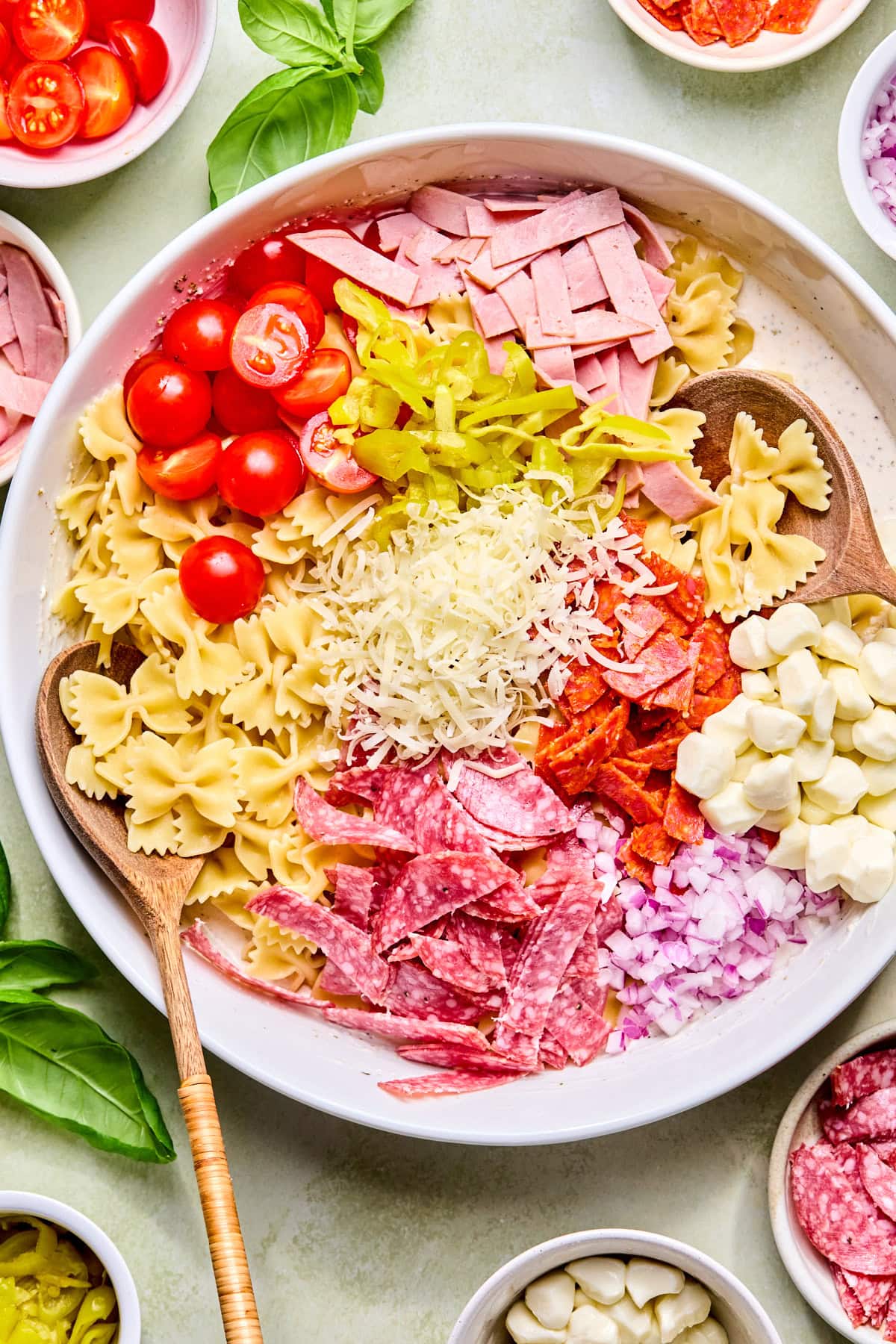 Cooled pasta, ham, salami, pepperoni, cherry tomatoes, banana peppers, red onion, mozzarella balls, and Parmesan cheese added to a large bowl before tossing with the dressing.