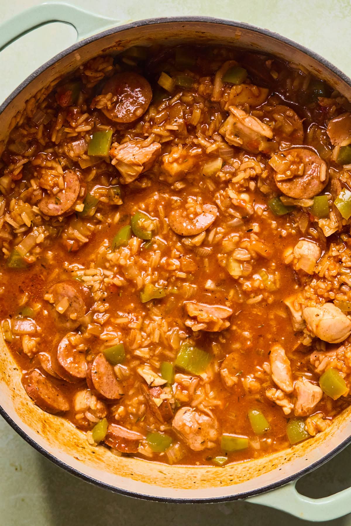 Browned chicken and andouille sausage returned to the pot with the rice mixture to simmer until the rice is almost tender.