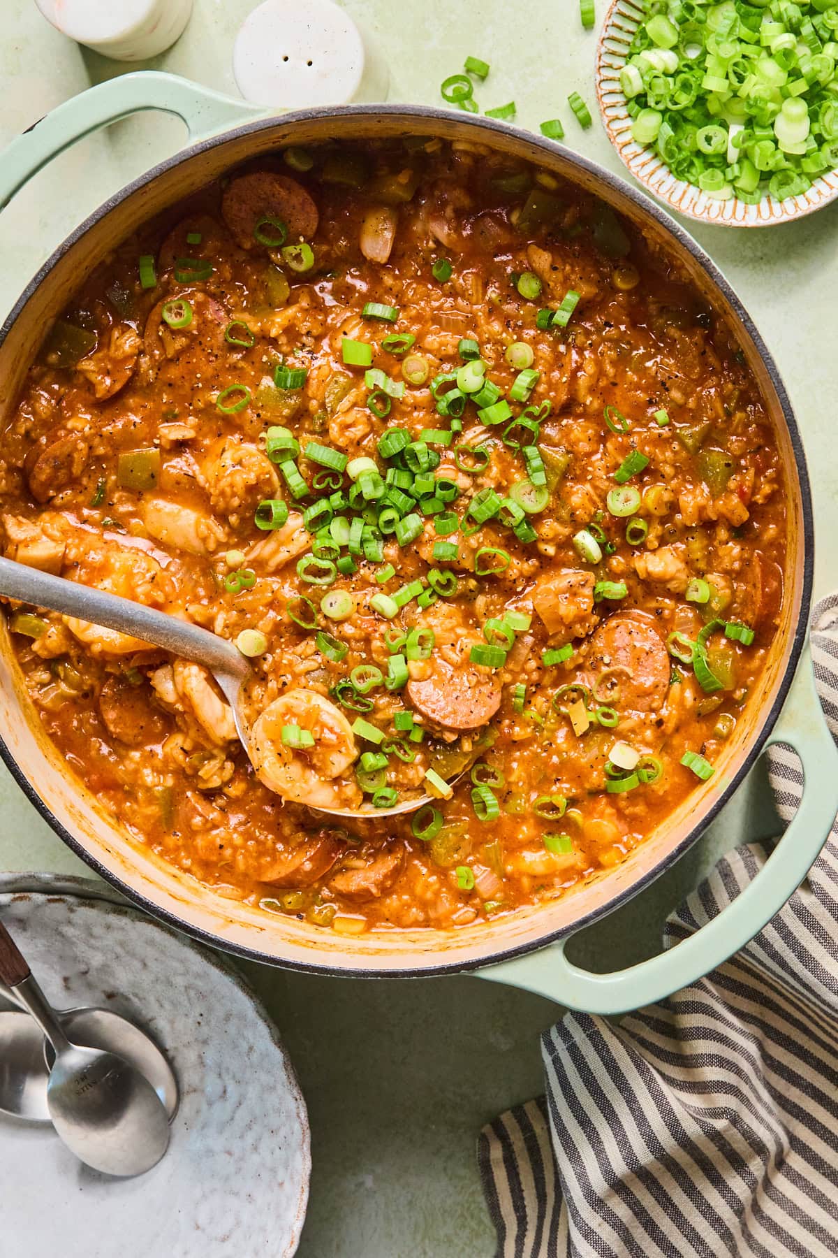Large pot of chicken and sausage jambalaya with shrimp, andouille sausage, rice, and green onions with a serving spoon.