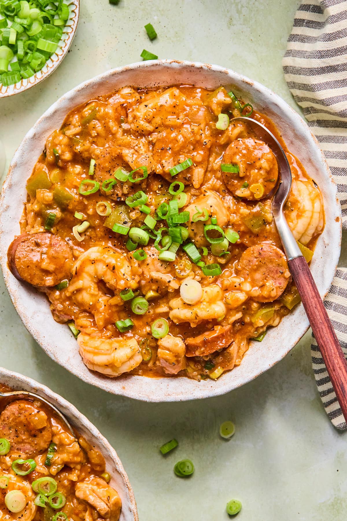 Bowl of chicken and sausage jambalaya with shrimp, andouille sausage, rice, and green onions, served with a spoon.