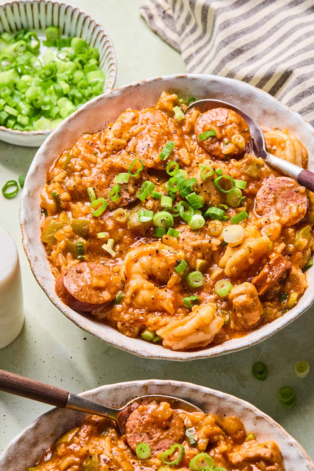 Two bowls of chicken and sausage jambalaya with shrimp, andouille sausage, rice, and green onions, served with spoons.