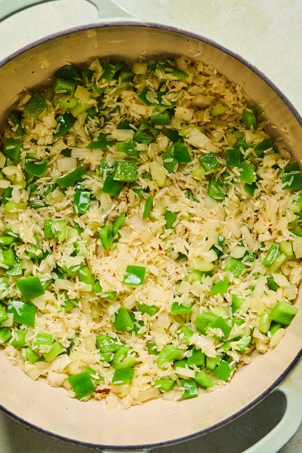 Butter, onion, celery, and bell pepper cooking in the same skillet after the meat has been removed. Garlic and rice have been stirred in and are toasting with the vegetables.