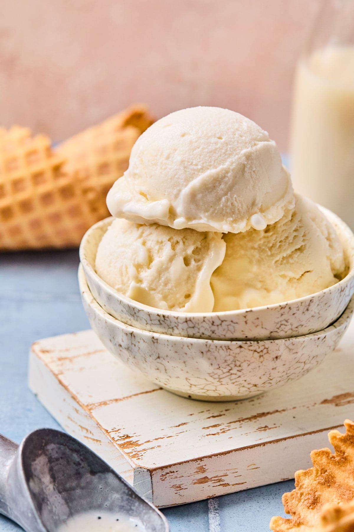Ninja Creami vanilla ice cream in a bowl on a white rustic cutting board with an ice cream scoop beside it.