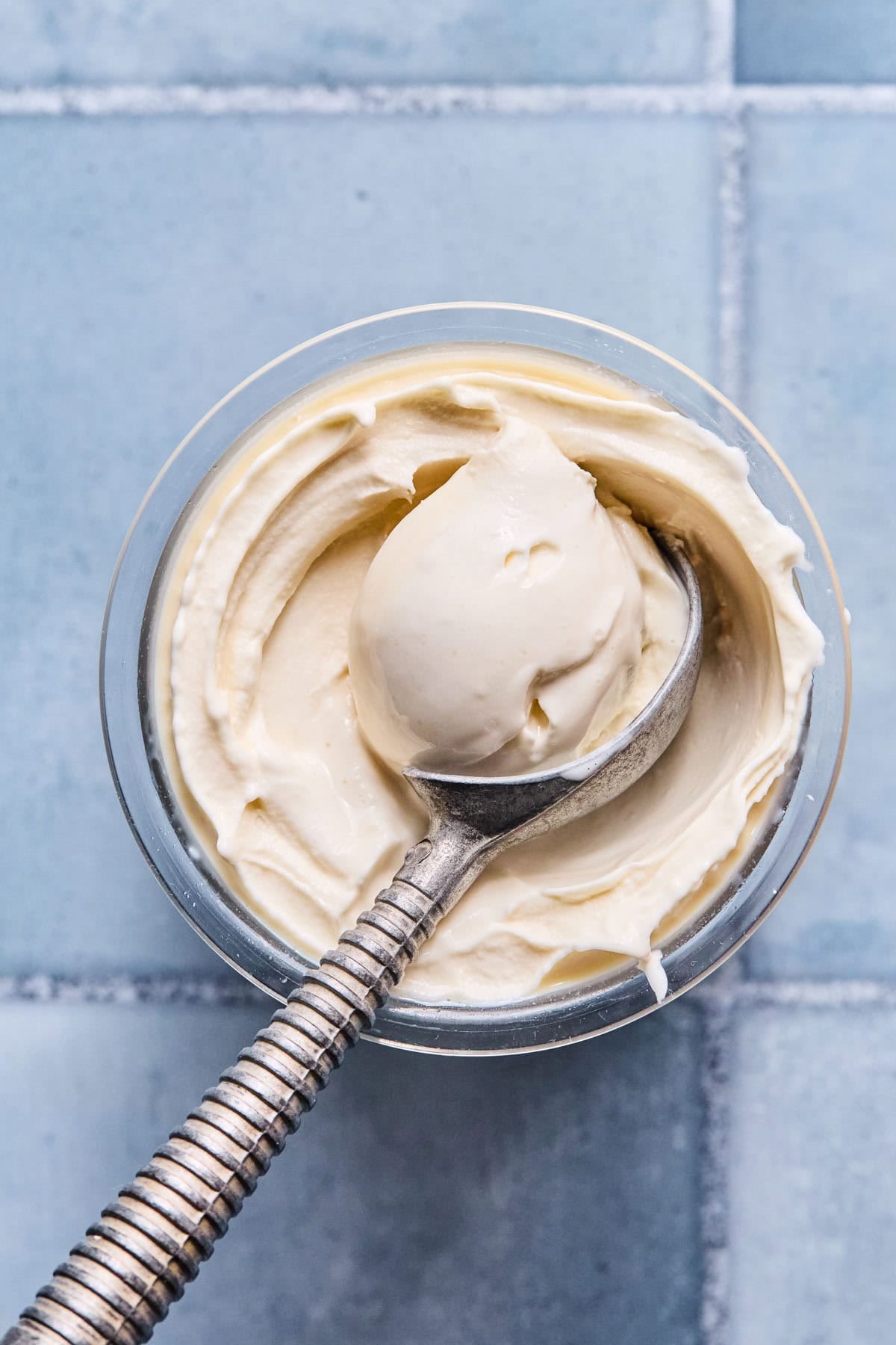 Finished Ninja Creami vanilla ice cream in the Ninja Creami pint container with an ice cream scoop scooping out a serving.