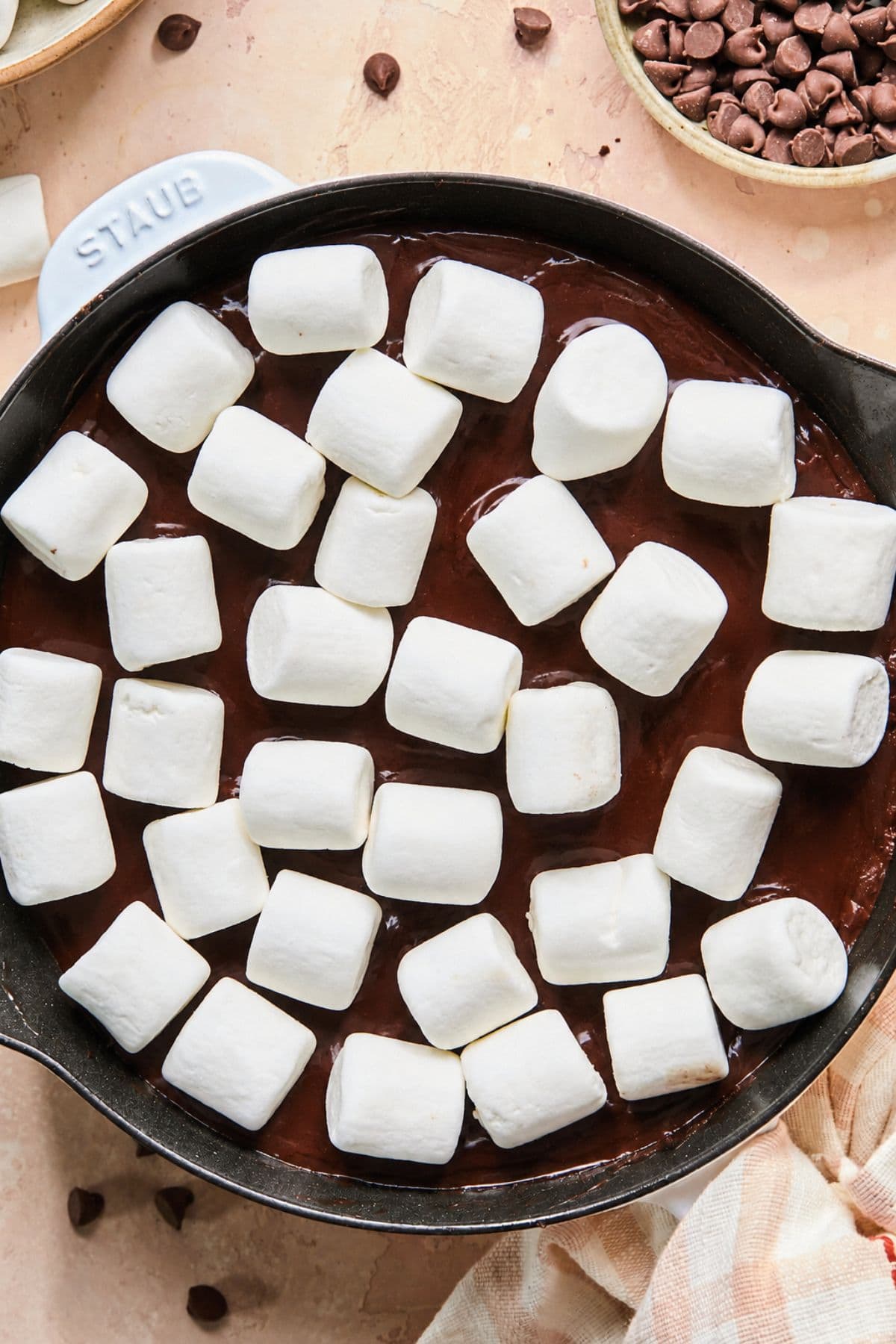 A cast iron skillet with melted milk chocolate chips, butter, and heavy cream with large marshmallows scattered on top.