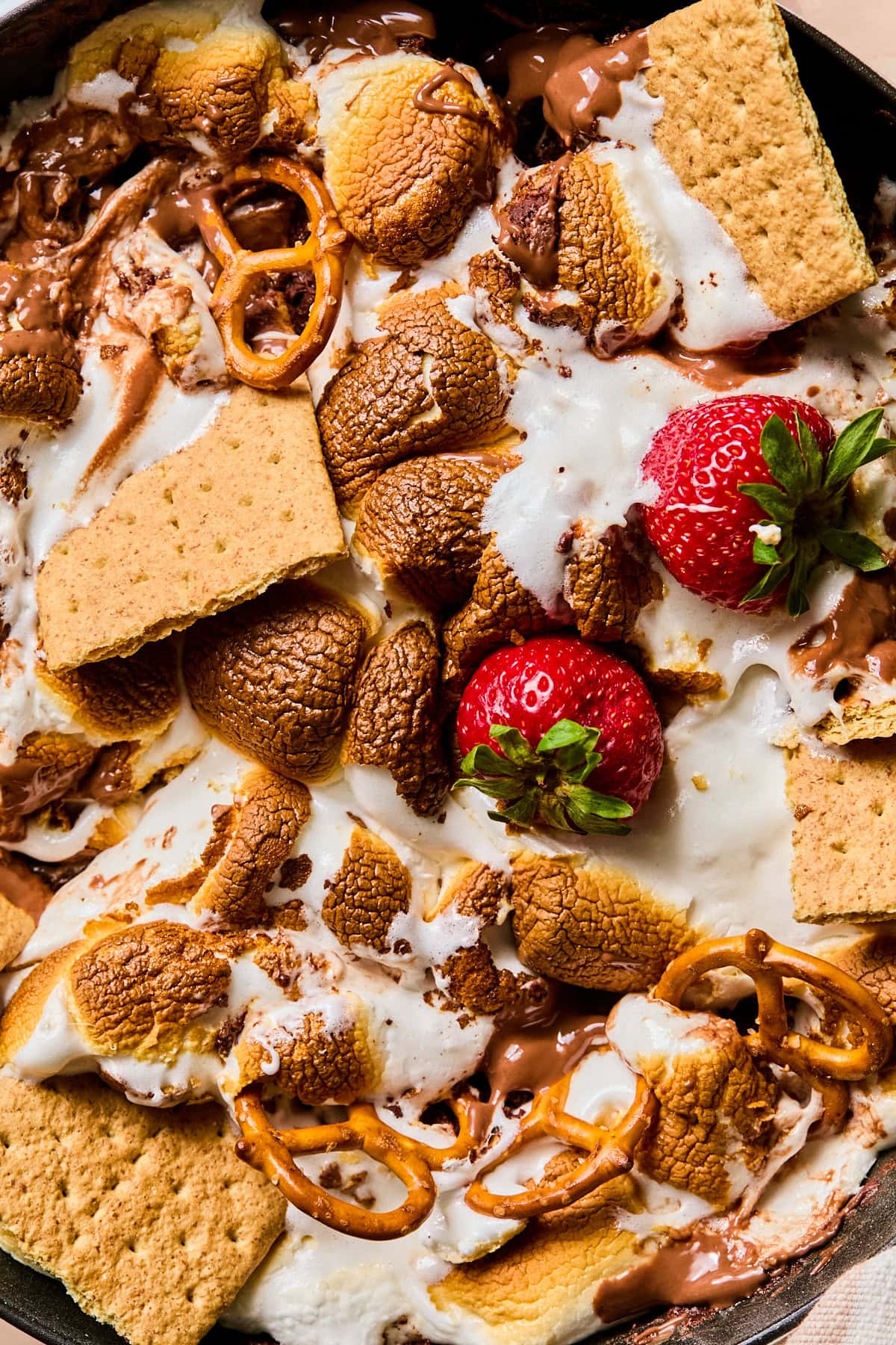Close-up of smores dip with pretzels, strawberries, and graham crackers in it.