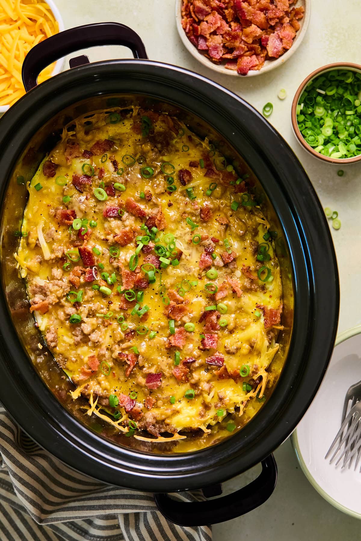 Breakfast casserole in a crockpot topped with crispy bacon and green onions.