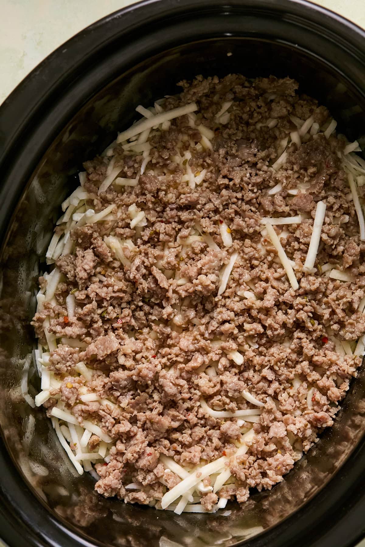 Browned sausage layered over frozen hash browns in a crockpot.