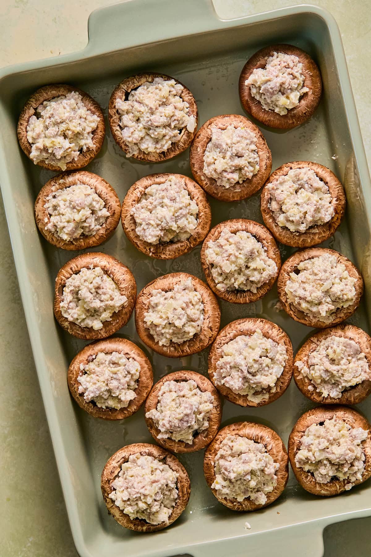 Mushroom caps filled with the creamy sausage mixture and arranged in a single layer in a baking dish.