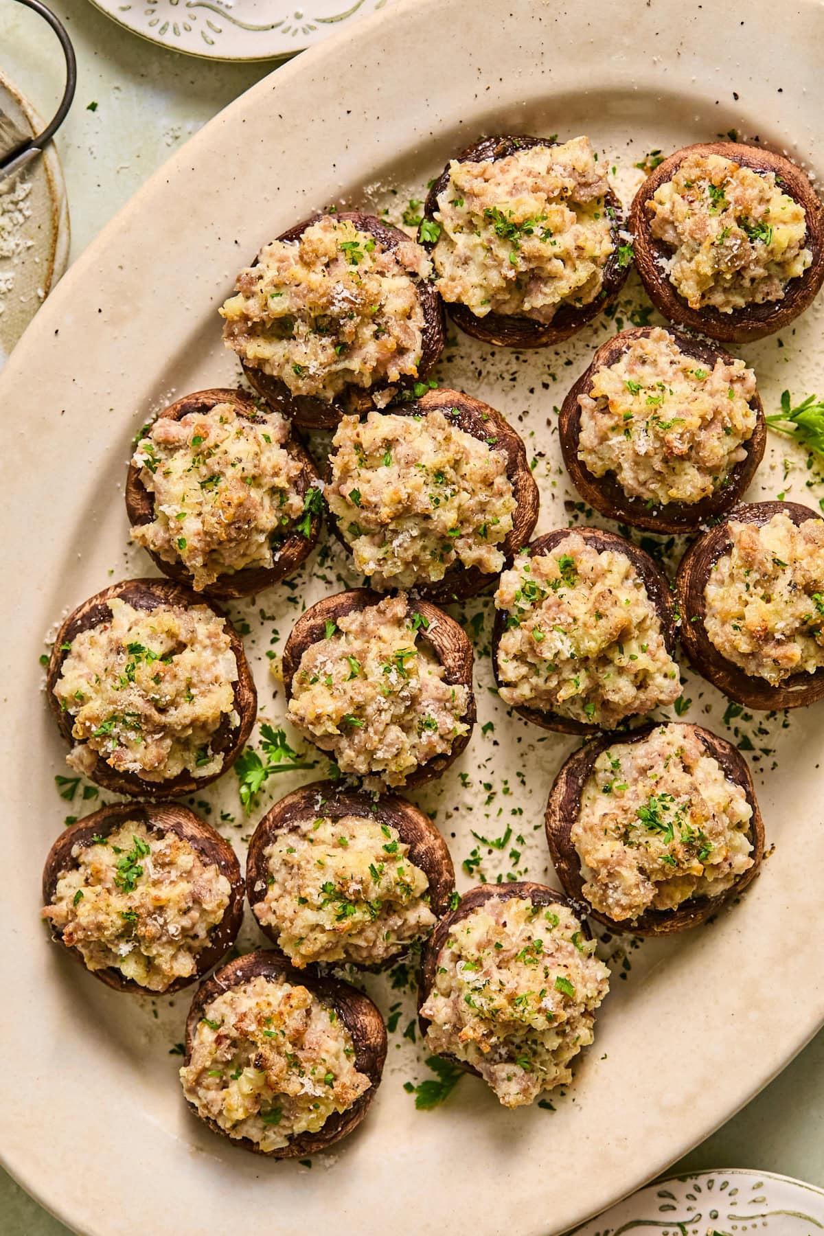 Sausage stuffed mushrooms garnished with fresh parmesan and parsley arranged on a serving platter.