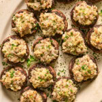 Sausage stuffed mushrooms garnished with fresh parmesan and parsley arranged on a serving platter.