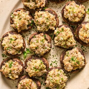 Sausage stuffed mushrooms garnished with fresh parmesan and parsley arranged on a serving platter.