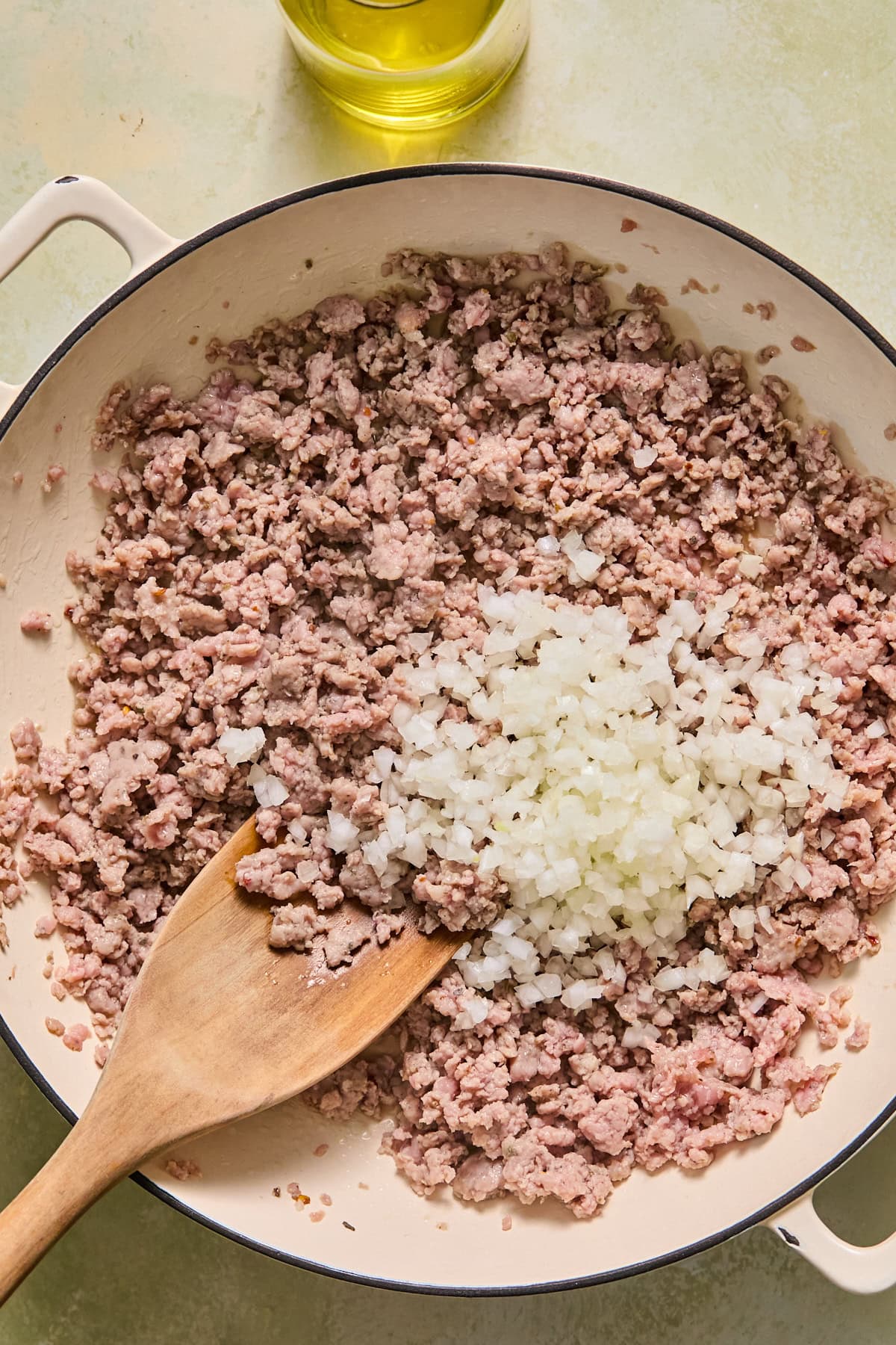 Large skillet with olive oil and crumbled breakfast sausage topped with chopped onion, ready to be stirred and cooked.