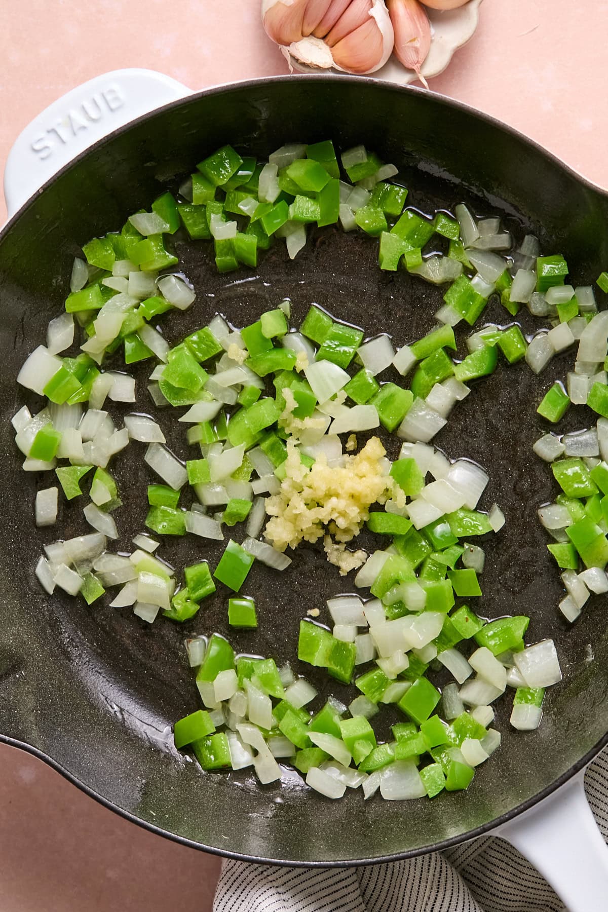 Onion and green bell pepper sautéing in butter and bacon grease in a skillet until softened, with garlic ready to stir in.