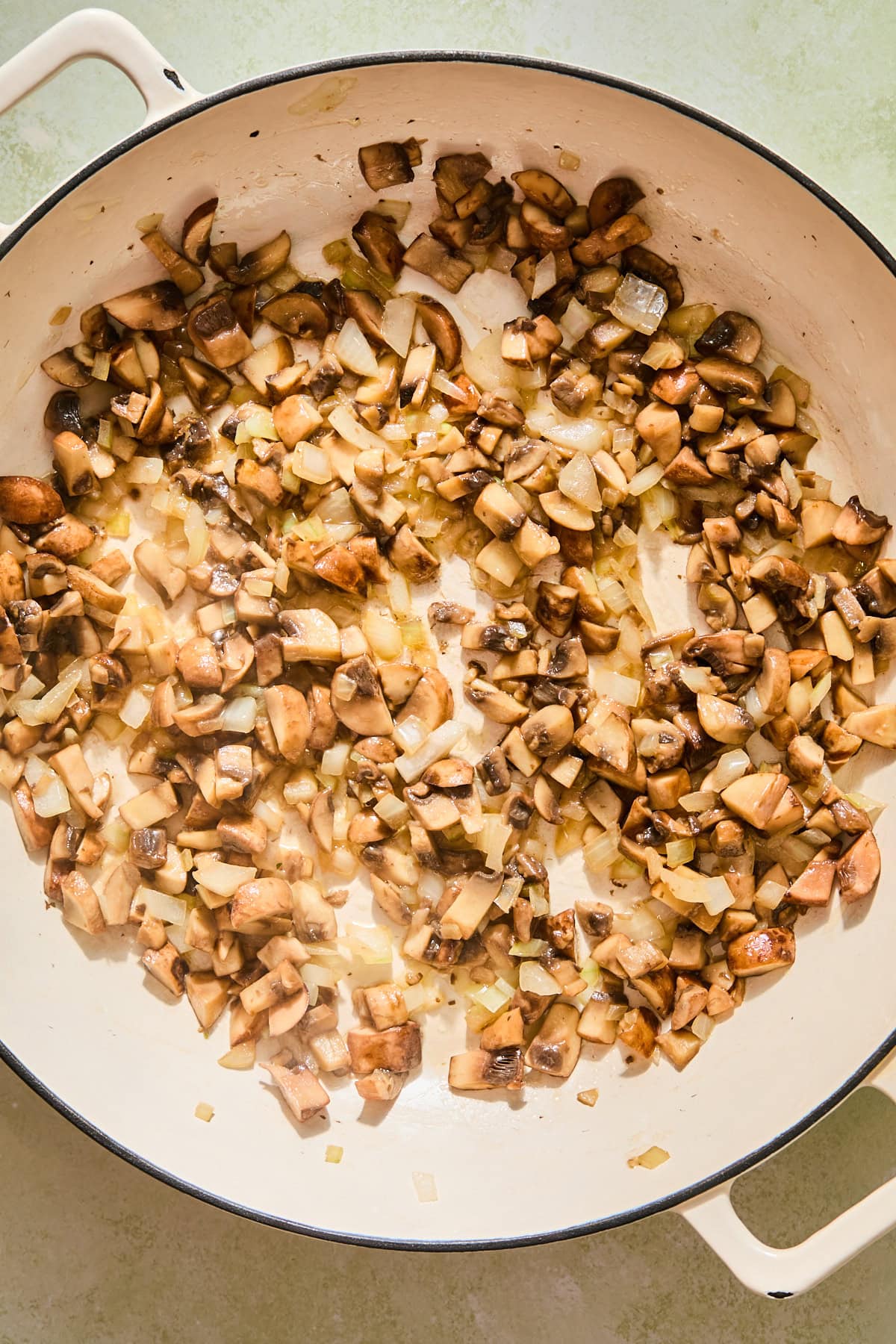 A pan with diced onions and mushrooms sauteeing until soft.