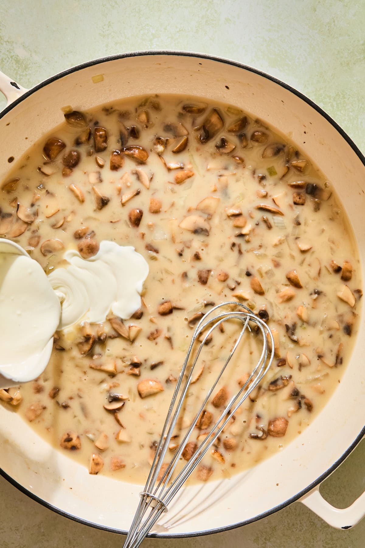 Whisking broth and heavy cream into the mushroom sauce in a skillet.