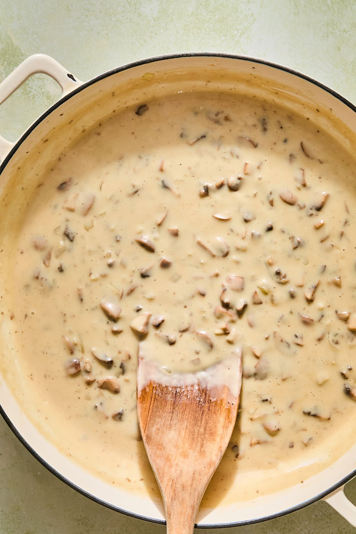 Creamy mushroom sauce simmering in a pan with a wooden spoon.
