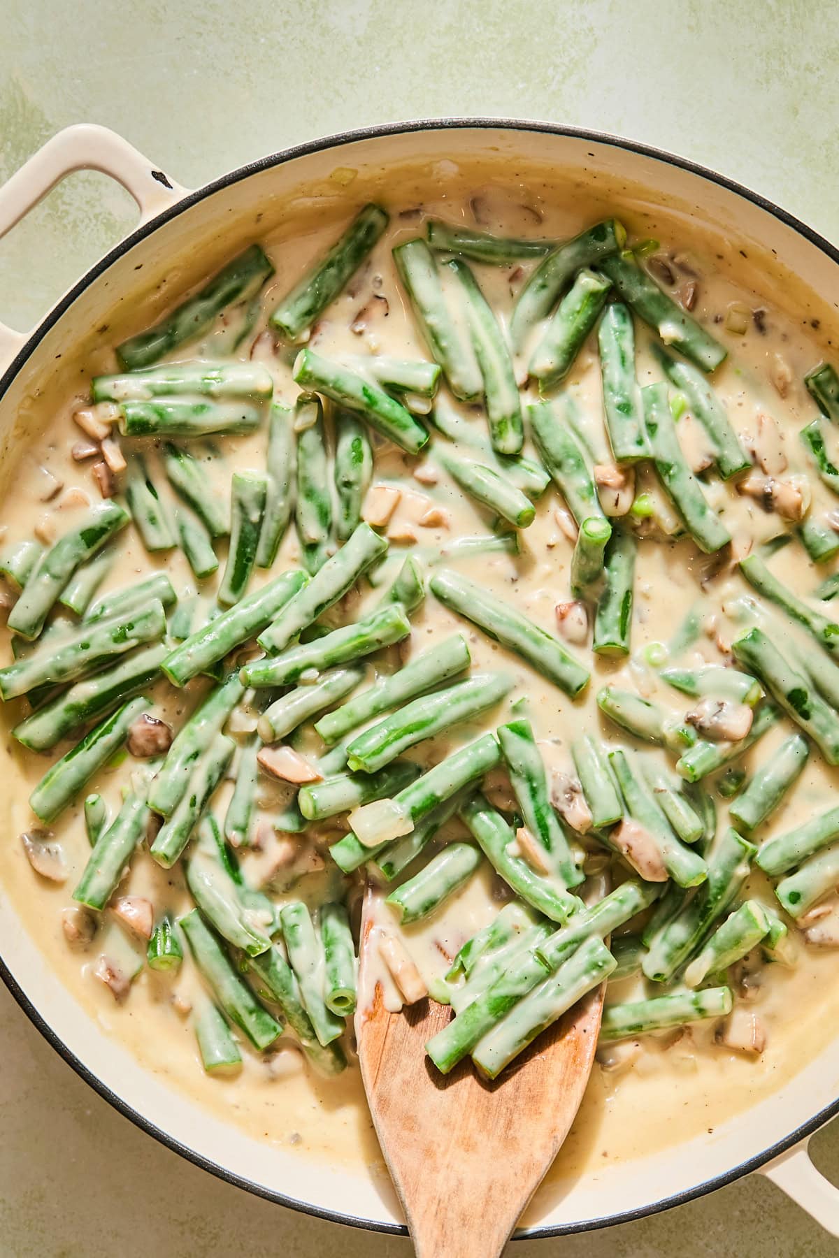 Gently stirring the blanched green beans into the pan with the mushroom sauce.