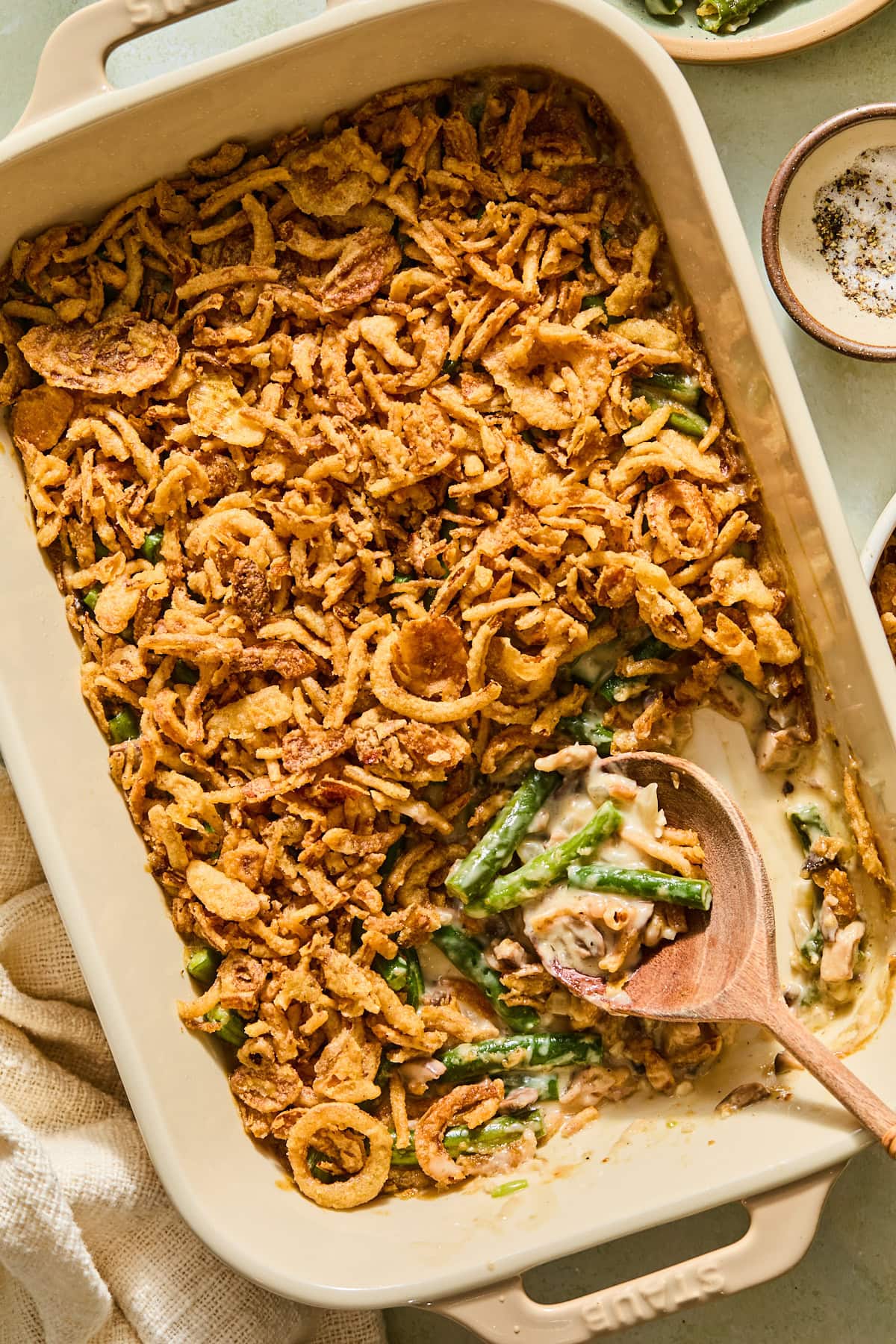A casserole dish filled with homemade green bean casserole topped with crispy fried onions, with a large helping scooped out of the pan.