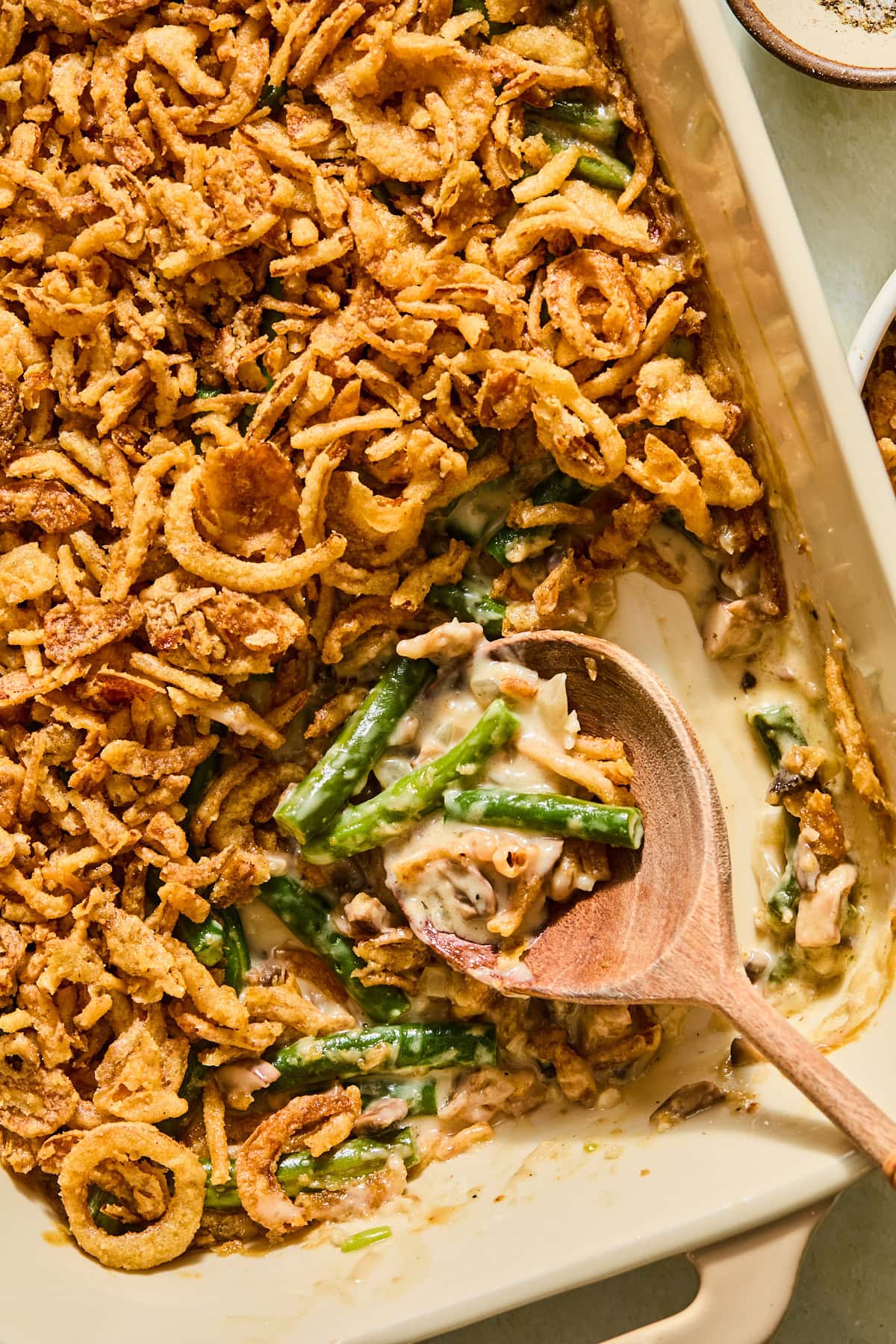 Scooping out the cooked green bean casserole with a wooden spoon.