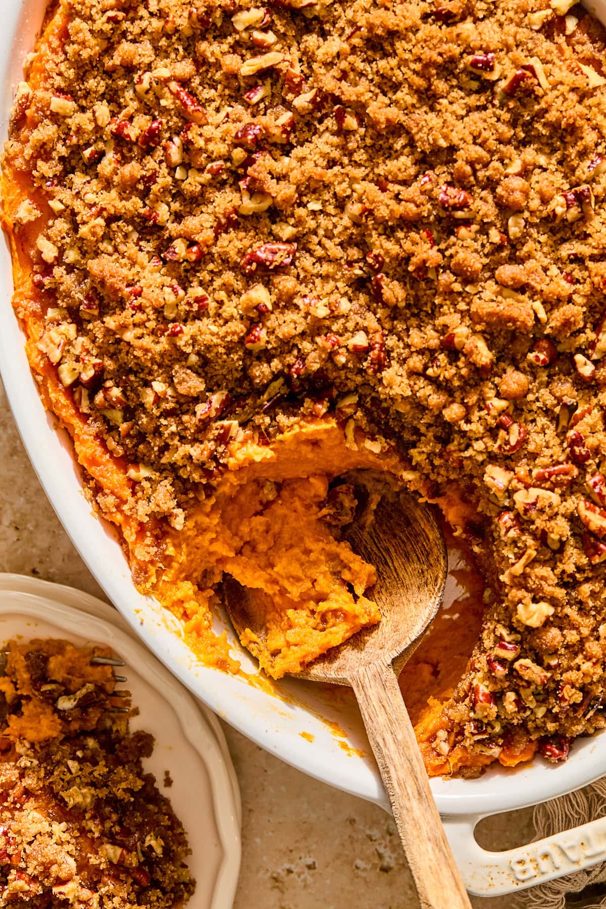 A sweet potato casserole with a hefty scoop taken out with a wooden spoon.