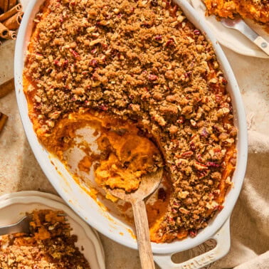Sweet potato casserole in a white, oval baking dish topped with pecans.