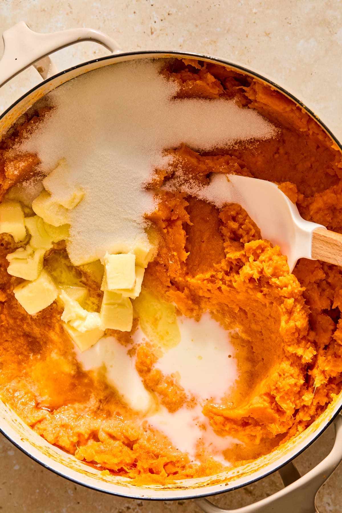 Adding butter and sugar to the mashed sweet potatoes to form the sweet potato casserole filling.